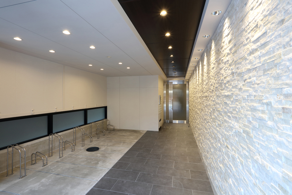 エントランス・駐輪場<br>壁面には凹凸のある石張りを採用。光をあてると、陰影が出て高級感ある雰囲気に