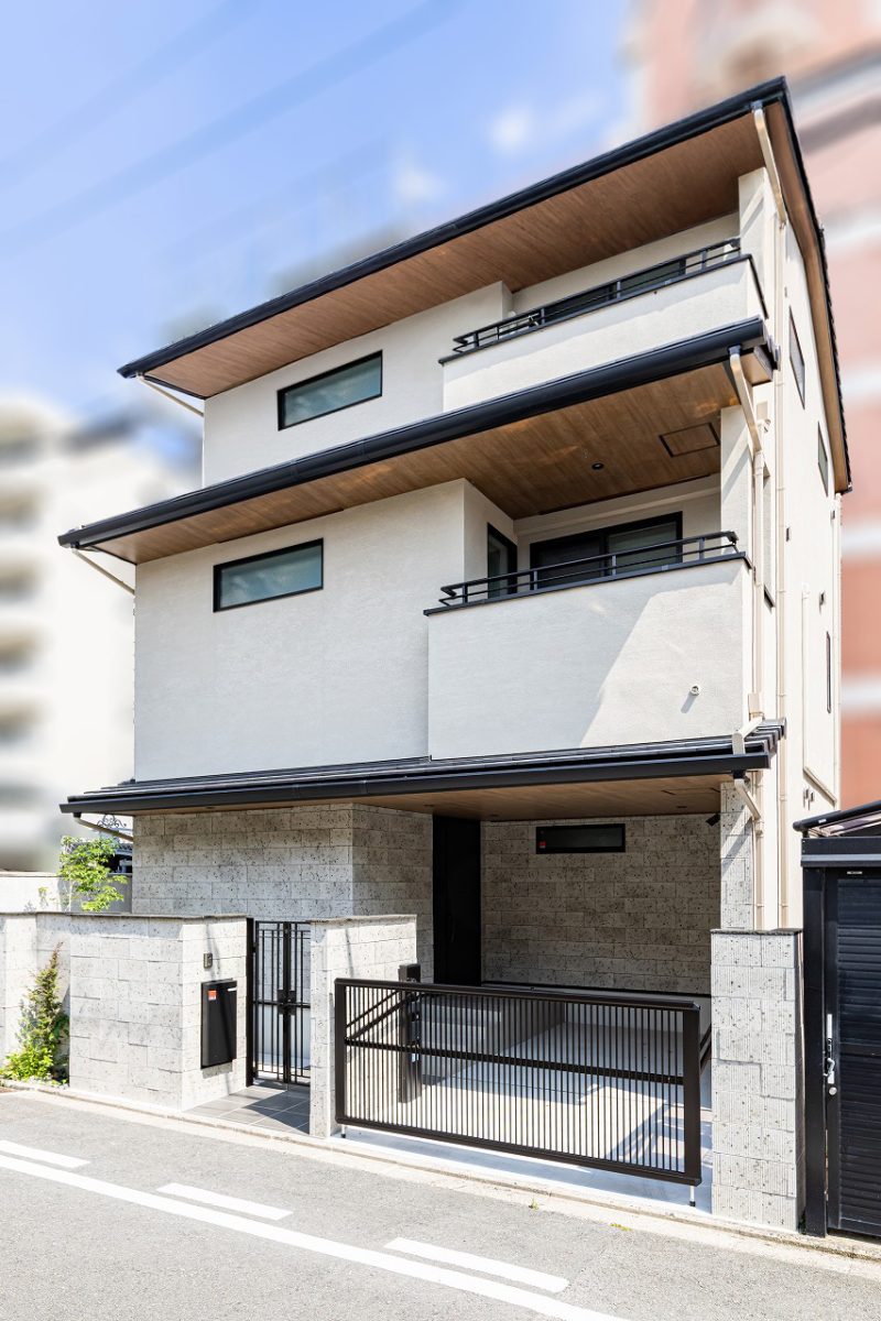 水平ラインが美しい、端正な佇まい。<br>奥行きのあるインナーバルコニーが、建物全体の水平ラインをより美しく見せています。軒天の木目と植栽の緑が映える、上質な仕上がりです。<br>外構門扉と外壁には大谷石調のタイルを採用し、建物と美しく調和するアプローチに。玄関は通りから直接見えないように配置し、プライバシーに配慮しました。