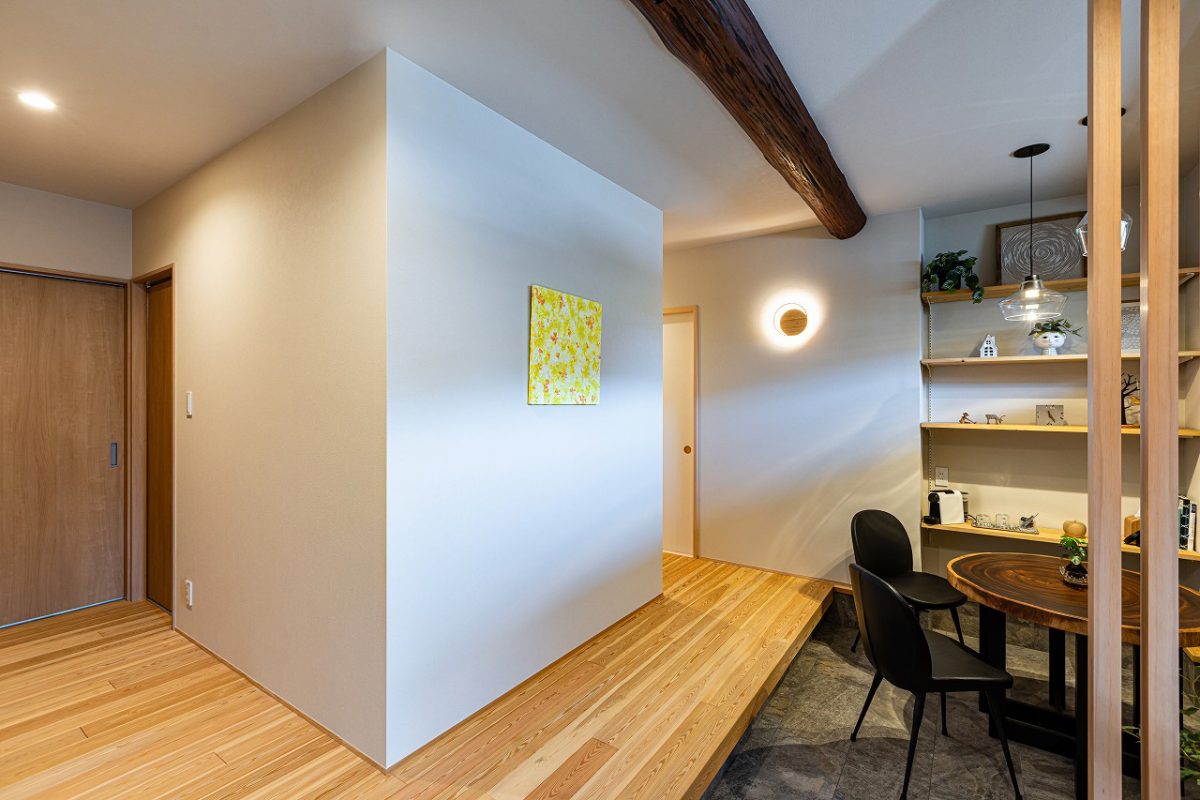 和モダンな玄関ホール。土間には石目調タイル、ホールには無垢材の床を採用し、素材のコントラストが心地よい空間に。化粧梁は建替え前の住まいで使われていた梁を再利用。温もりと想い出が息づく玄関です。<br>また、サニタリースペースを中心に、左手は寝室、右手にはLDKと和室へとつながる回遊動線で、日々の暮らしやすさに配慮した設計です。　