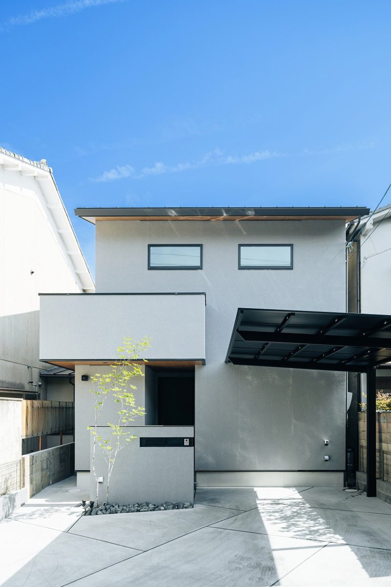 グレーを基調とした、シンプルモダンな外観。無駄を削ぎ落とした直線的なデザインに、木目と植栽がアクセントになっています。<br>奥まった位置に設けた玄関は、通りからの視線をほどよく遮り、プライバシーに配慮された設計です。