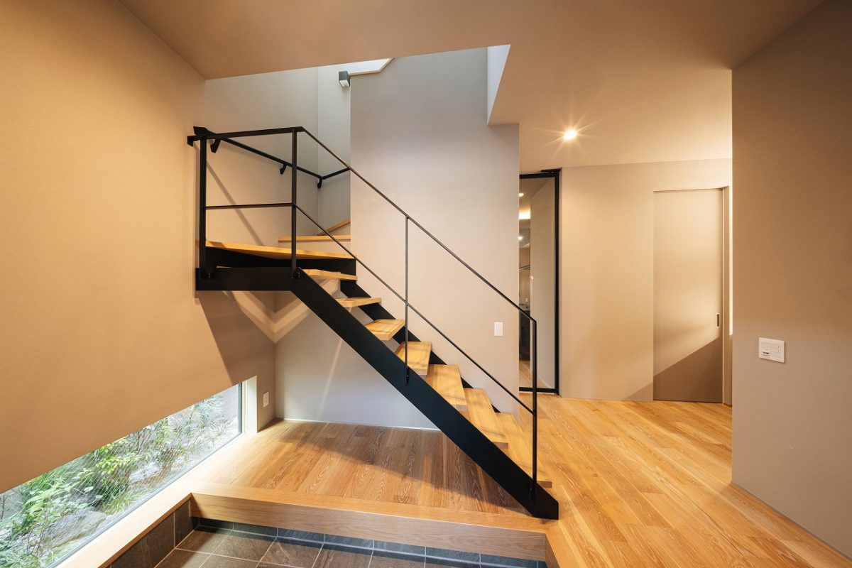 木とグレーでまとめた玄関ホール。2階に続く階段は、一部鉄骨階段にして抜け感を作りました。<br>階段上部の吹き抜けからは、玄関ホール全体に光が差し込みます。<br>地窓からはやさしい光が差し込み、外の植栽をさりげなく楽しむことができます。