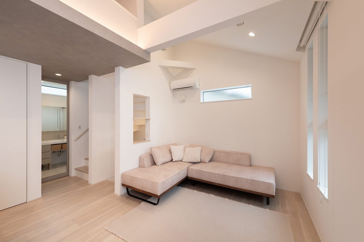シンプルでモダンなインテリアが特徴のリビングルームです。明るいベージュのソファとカーペットが調和し、温かみを加えています。<br>勾配天井で開放感を演出し、壁にはくりぬきニッチがアクセントになり、空間に抜け感を与え、広々とした印象を与えます。