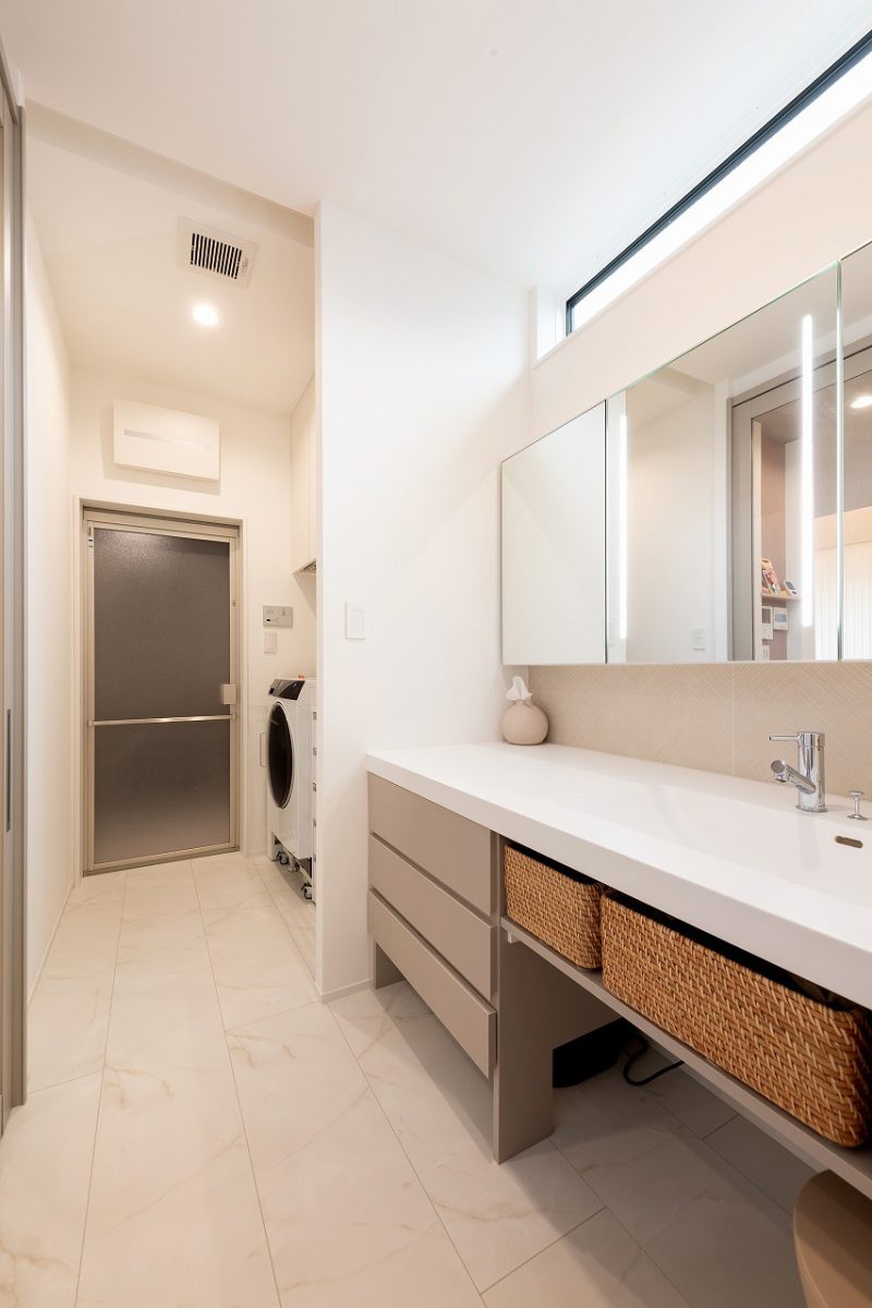 上部の窓から入る自然光によって明るい雰囲気が作られ、全体的にベージュでまとめることで、柔らかな印象にしています。<br><br>ゆったりとお化粧ができるよう椅子を置けるスペースをつくり、お掃除ロボットの基地としての機能も備えていることで、ライフスタイルに合わせた造作洗面台を設計しています。さらに、大容量の引き出し収納が完備されており、洗面道具や小物類をすっきりと収納することができます。