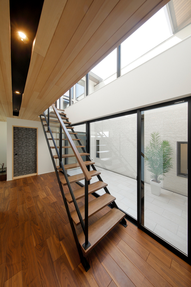 階段を取り込んだ吹き抜けを中庭に隣接させ、窓を全面にとることで玄関ホール～中庭～空へと繋がる開放的な空間を演出しました。<br>奥行きの深い敷地でも、中庭からの採光で各部屋明るくなりました。