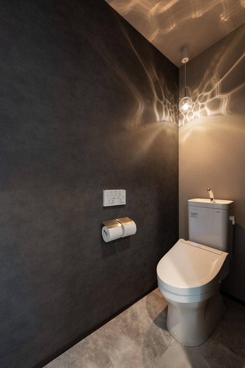 ホテルライクで落ち着いた雰囲気のトイレ。深みのあるダークグレーの壁と大理石調の床材で、品のある印象に仕上げました。ペンダントライトがやわらかな光を広げ、壁に映る陰影が美しいアクセントになっています。