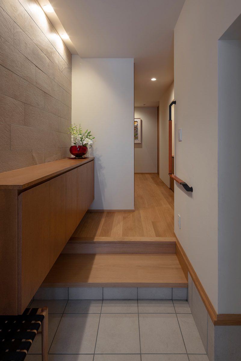 将来を見据え、玄関の幅は車椅子が入るゆとりを持たせ、緩やかな段差に設計。L字形の手すりはヌメ革でカバーされたエレガントなデザインです。