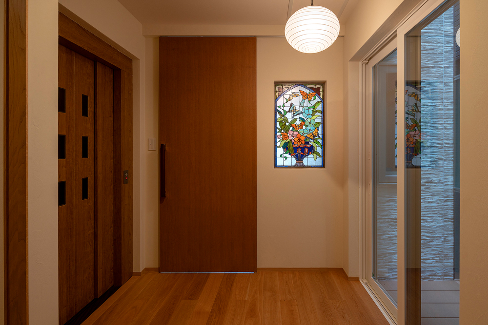 ギャラリーのような玄関ホールの奥がお母さまの部屋。左手にはエレベーターを、右手には坪庭を配しました。壁に施したステンドグラスはもともとお持ちだったもの。