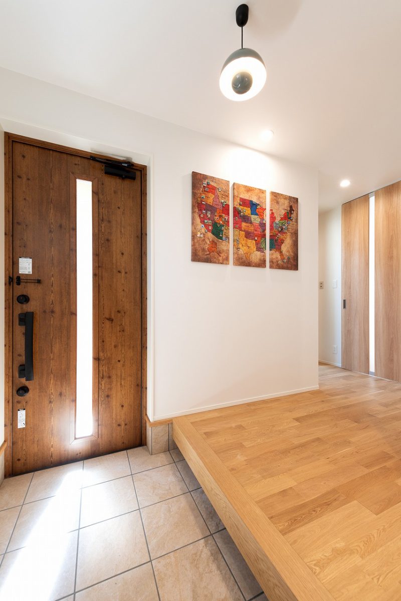  玄関は道路に面さないように配置し、プライバシーに配慮した設計に。<br>広々とした玄関ホールにはお施主様お気に入りのアートパネルが飾られています。<br>内観はナチュラルなテイストで統一し、リビングに繋がる扉はハイドアを採用することで、空間に奥行きを感じさせます。<br>玄関横にシューズクロークを設け、常に玄関をすっきりと見せることができます。
